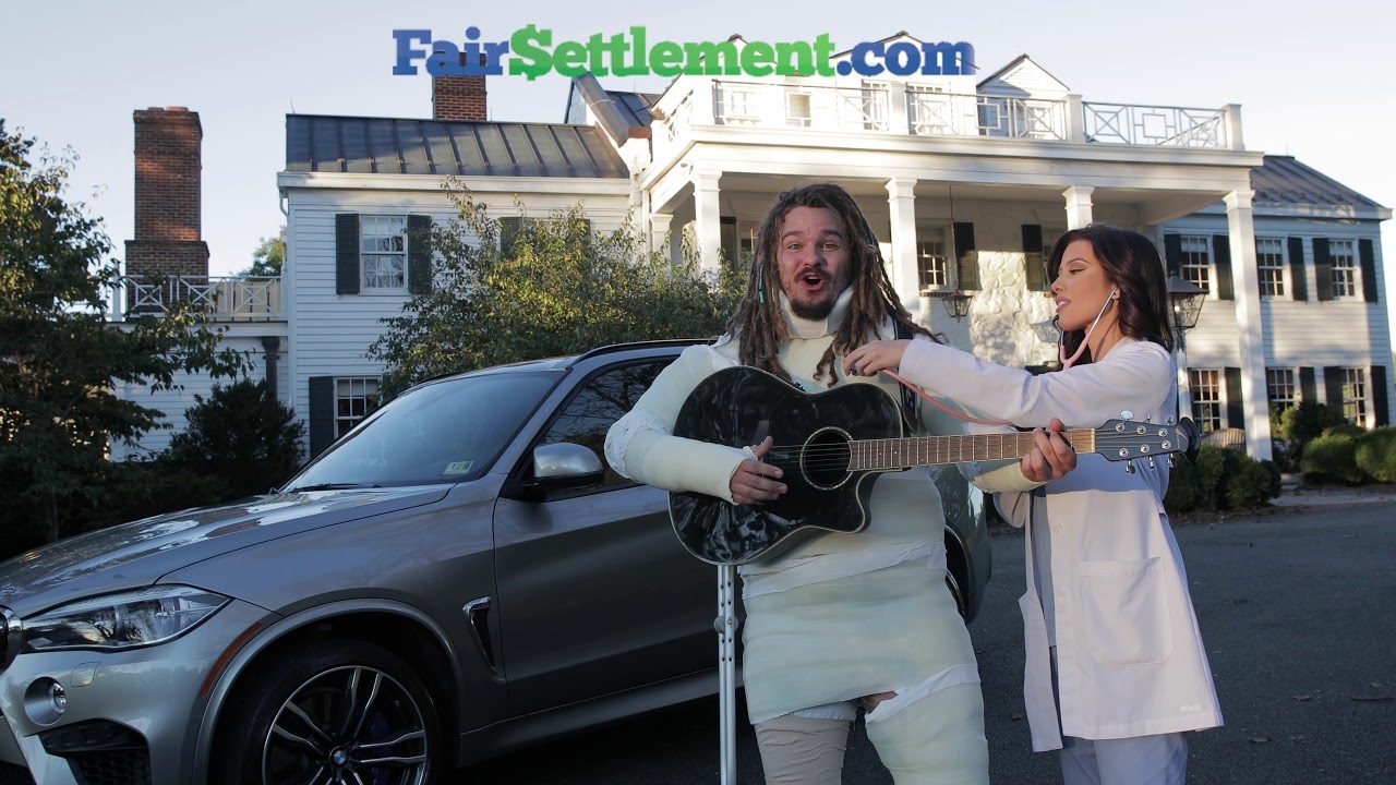Still from the FairSettlement.com commercial: a man in casts playing guitar next to a woman in a doctor's coat in front of a white house