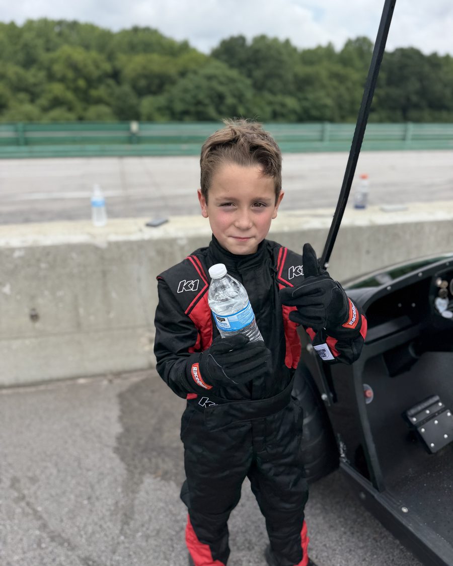 One of Brent Lillard's sons in a K1 race suit next to the car at the track